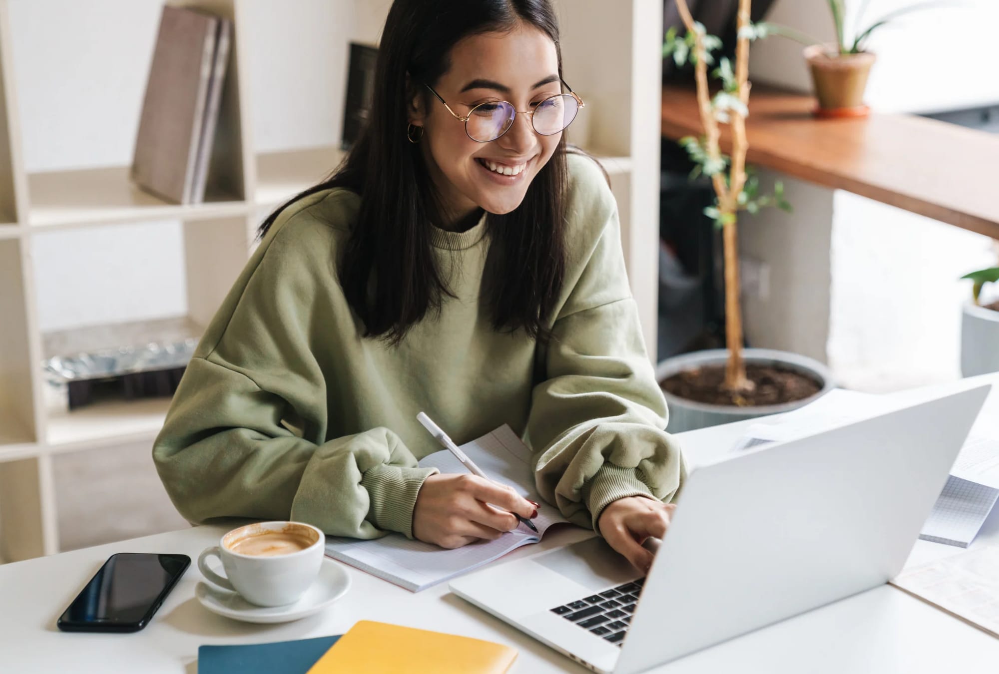 Woman writing in a journal while working on her laptop